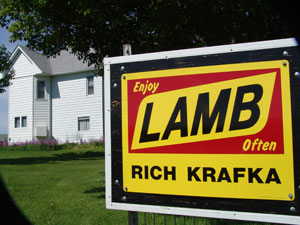 Sign reading 'Enjoy Lamb Often - Rich Krafka' in front of a white house